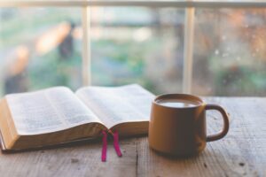 An open Bible and a cup of coffee by a window